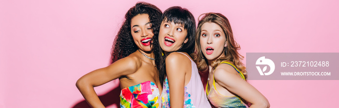 panoramic shot of beautiful fashionable multicultural girlfriends posing on pink