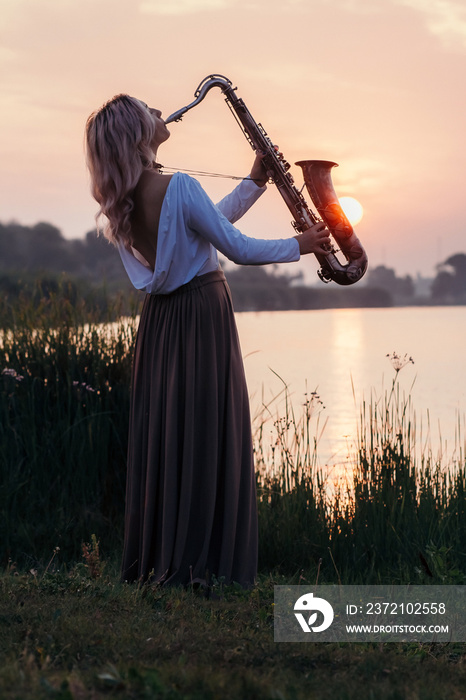 silhouette of a young beautiful girl playing the saxophone at sunrise by the river, a woman in a lon