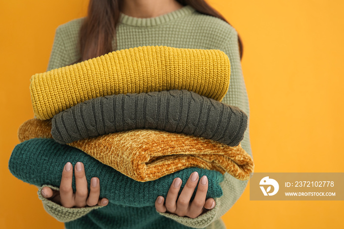 Woman with beautiful manicure holding stack of warm sweaters on color background