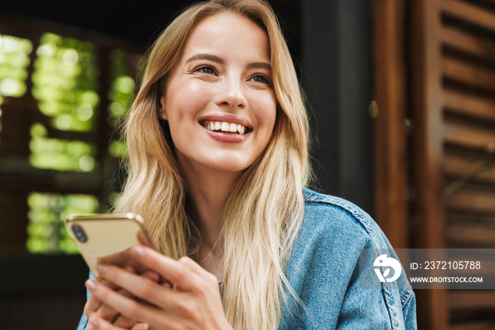 Amazing woman posing outdoors in cafe using mobile phone.