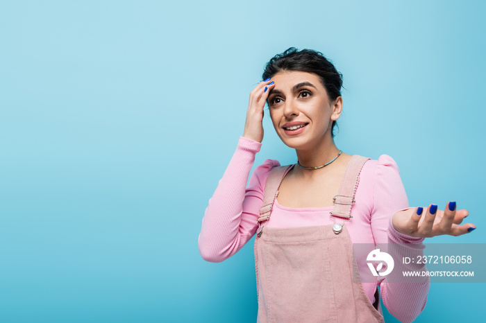 forgetful woman touching head and pointing with hand while thinking isolated on blue