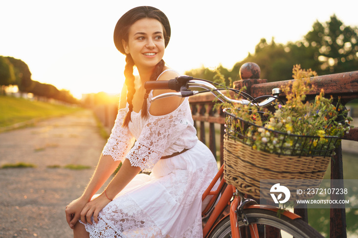 Young beautiful woman sitting on her bicycle with flowers at sunset