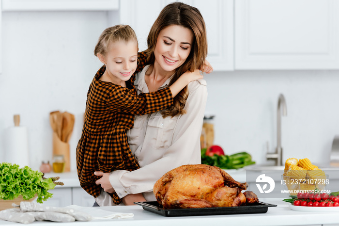 美丽的年轻母女在一起烹饪感恩节火鸡时拥抱