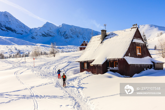 冬季，两名滑雪者走过塔特拉山脉美丽的加西尼科瓦山谷的小屋