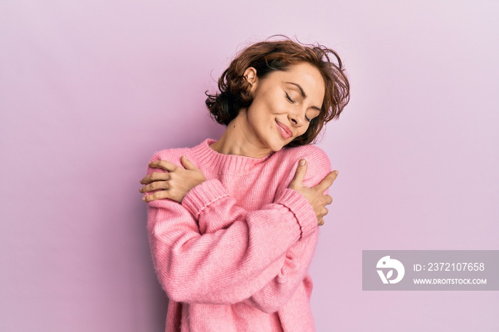 Young brunette woman wearing casual winter sweater hugging oneself happy and positive, smiling confi