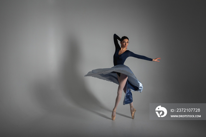 young pretty, fragile, beautiful ballerina dancing in a long blue dress on a uniform background, low