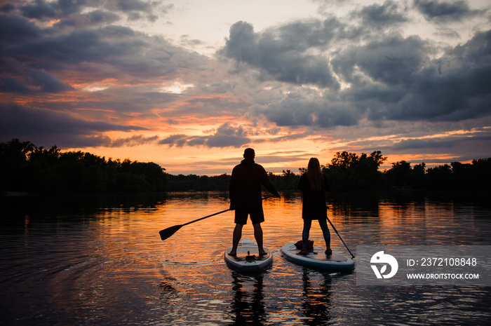 romantic view on man and woman on sup boards floating on river