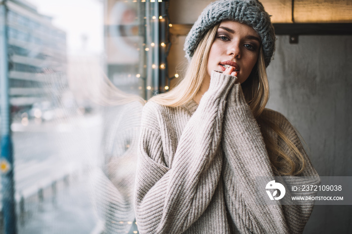 Half length portrait of trendy dressed hipster girl in knitted winter hat and pullover looking at ca