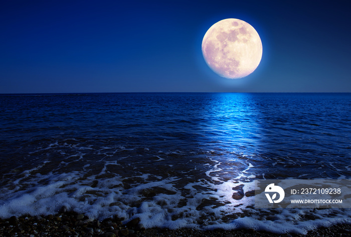 Full moon with reflections on a calm sea at midnight.