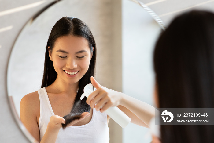 Happy long-haired young korean woman using hair spray