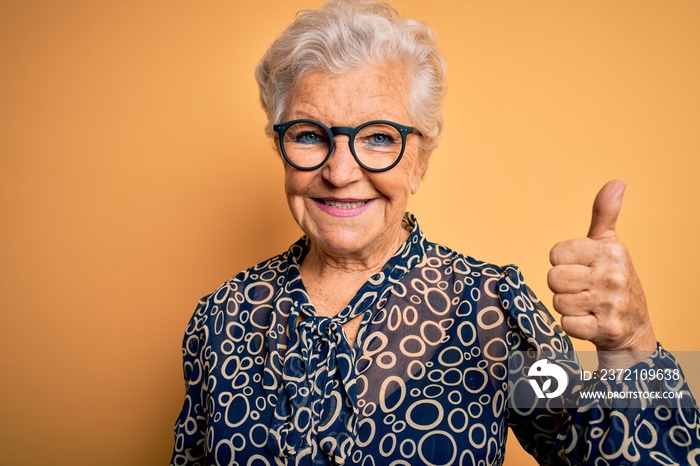 Senior beautiful grey-haired woman wearing casual shirt and glasses over yellow background doing hap
