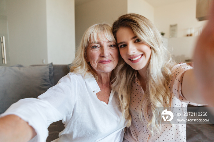 Cheerful lady on sofa with grandmother hugging make selfie.