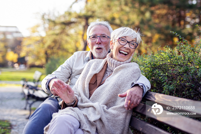 Mature couple sitting on bench in public park talk and smile