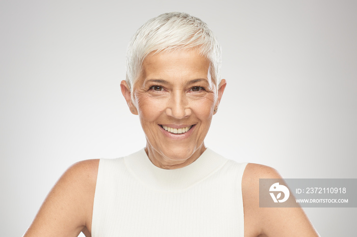 Beautiful smiling senior woman with short gray hair posing in front of gray background. Beauty photo