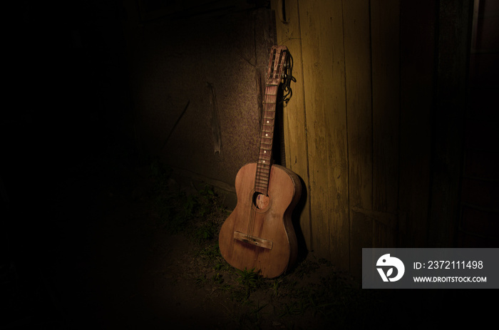 An wooden acoustic guitar is against a grunge textured wall. The room is dark with a spotlight for y