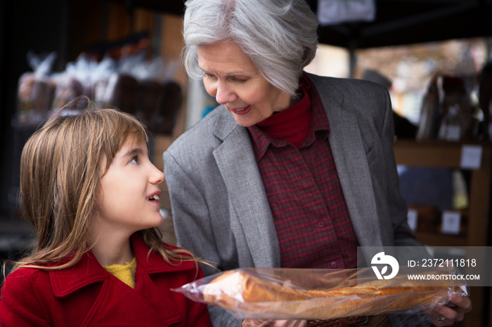 Grandmother with granddaughter (8-9) choosing baguette in bakery