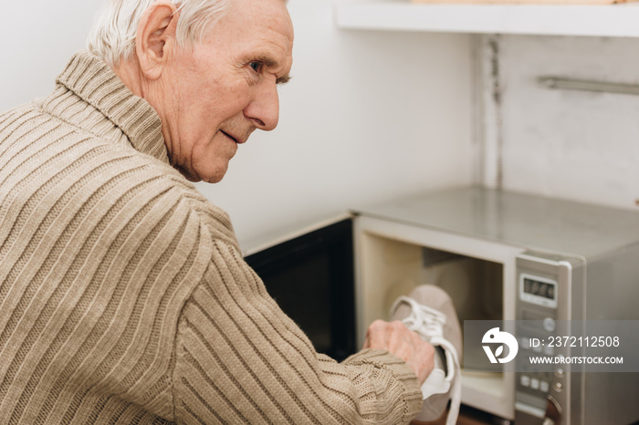 senior man with dementia disease putting shoe in microwave oven