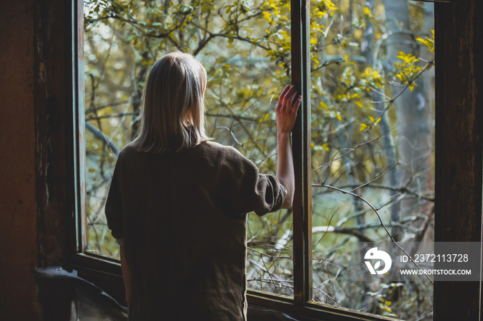 Woman stands with her back to the camera near window in a garden