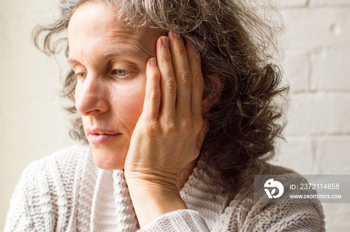 Middle aged woman in grey cardigan with hand on head, looking pensive (selective focus)