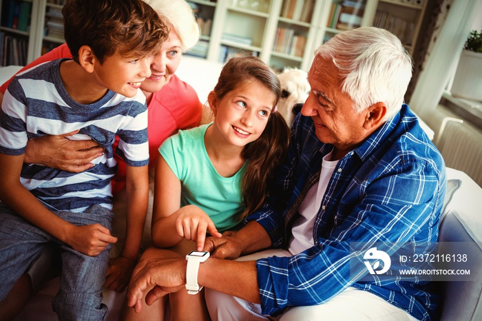 Grandparents and grandchildren looking at smartwatch in living