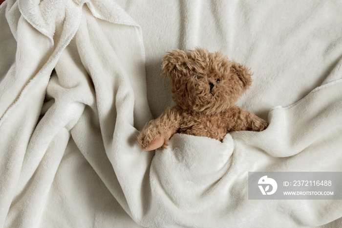 teddy brown bear lies in a white blanket on a wooden background close up, soft toy