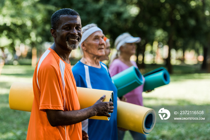 selective focus of positive retired african american man near pensioners holding fitness mats