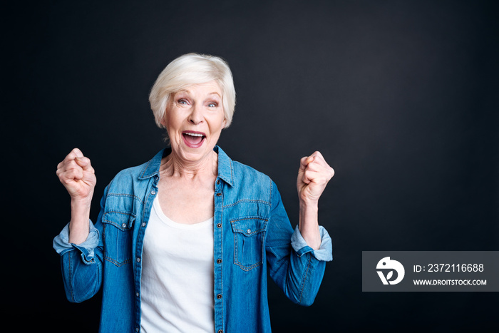 Delighted elderly woman standing on black background