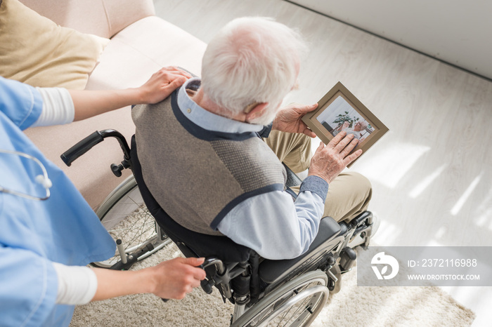 High angle view of nurse standing behind disabled gray haired man in wheelchair