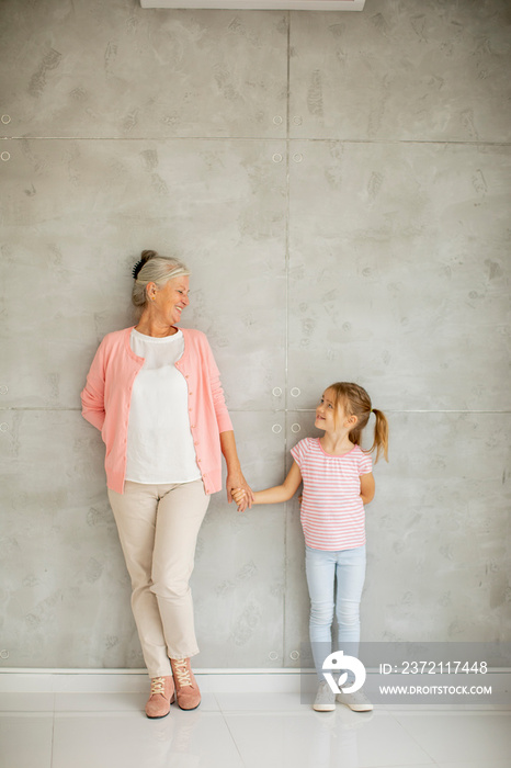 Little girl with her grandmother standing by the wall