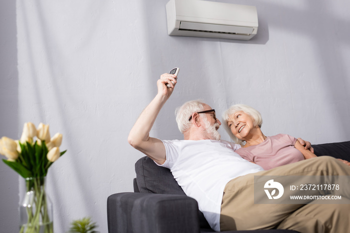 Selective focus of smiling man switching air conditioner with remote controller near wife