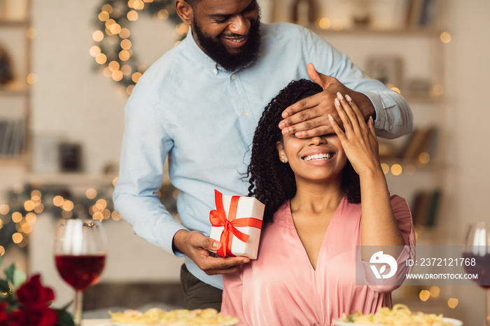 Young black man giving box to woman, covering eyes