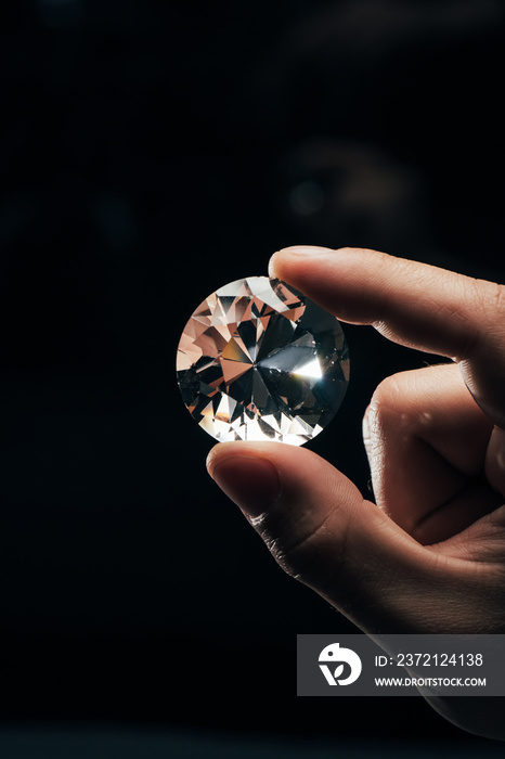 cropped view of man holding big clear shiny diamond on black background