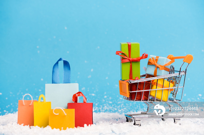 Tiny paper bags near trolley with bunch of little gifts on blue background, new year concept