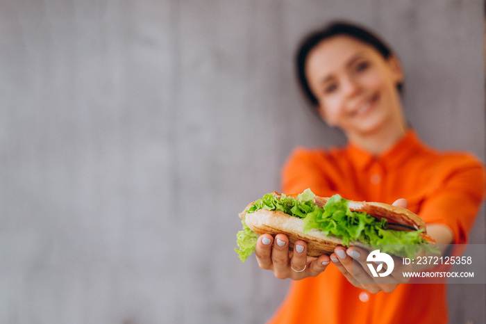 A beautiful, smiling woman in an orange shirt holds a sandwich in her hands. Focus on the sandwich, 