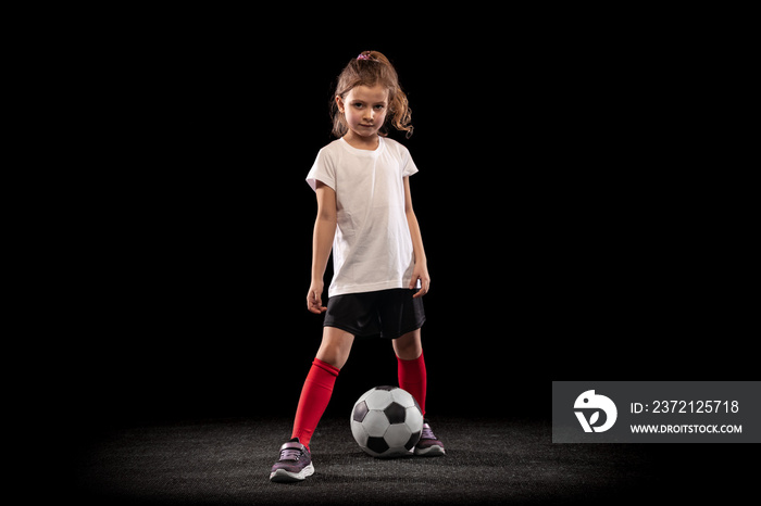 穿着足球服的小女孩在黑色背景下单独摆姿势的全长肖像