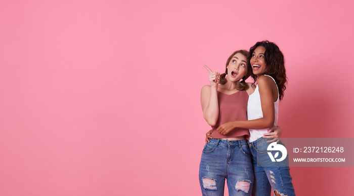 Portrait of two excited young woman standing with her finger pointing at copy space isolated over pi