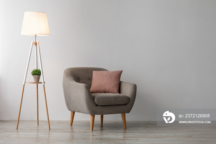 舒适的扶手椅，带粉色枕头，办公室或餐厅灰色墙壁背景上的地板上有发光的灯