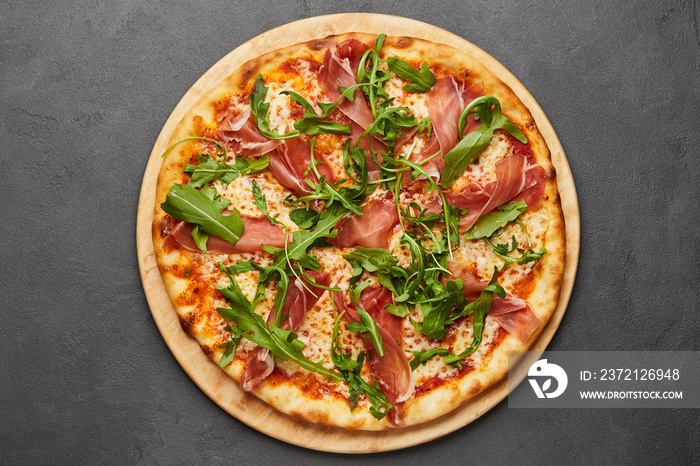 Delicious Italian Pizza with Parma ham and arugula, mozzarella cheese on dark background