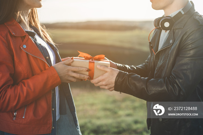 Gift of love. Close up of man giving present with red ribbon to woman on green meadow