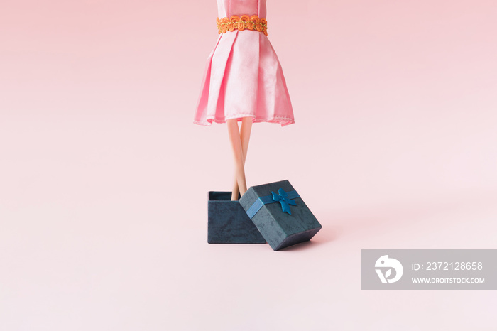 一个穿着粉色连衣裙的女人从蓝色礼盒里出来。背景是粉色。