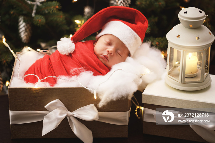 Cute newborn baby wearing Santa Claus hat is sleeping in the Christmas gift box