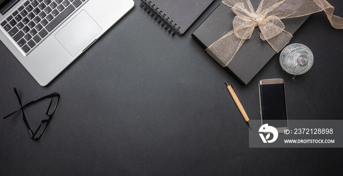 Black gift box with shiny ribbon on black office desk, top view