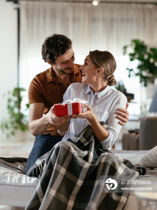 Husband surprising his wife with a gift. Young man giving a gift box to his wife