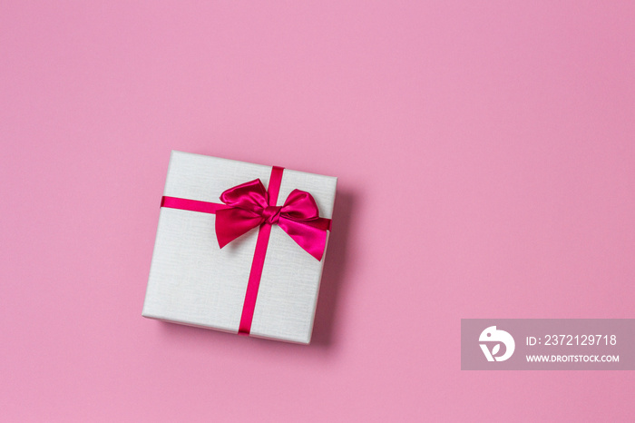 Gift present box with satin bow on light pink background, top view