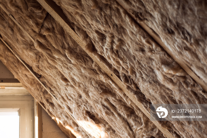 Glass wool and styrofoam in a wooden frame on a inclined wall near the wooden ceiling and a window i