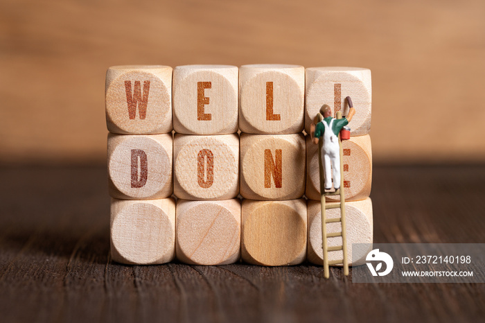 little painter figure and cubes showing the message  well done  on wooden background