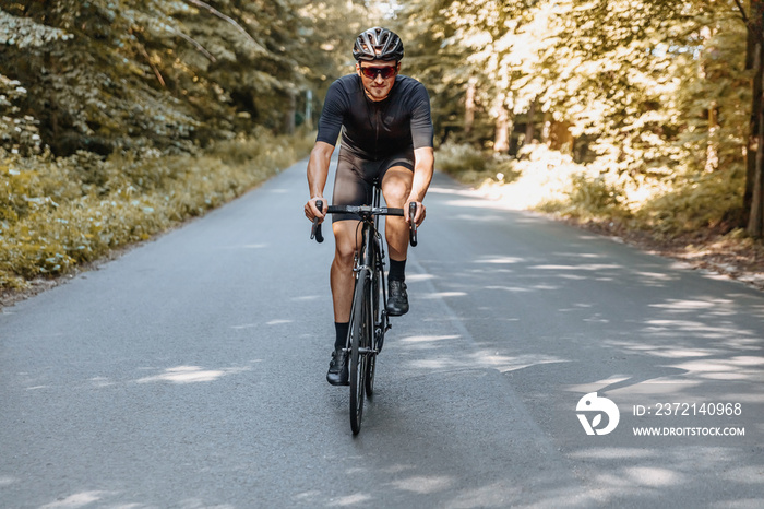 Happy mature man in sport clothing, protective helmet and mirrored glasses cycling among summer fore