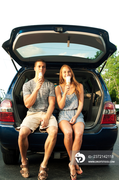 Couple sitting on car trunk eating ice cream