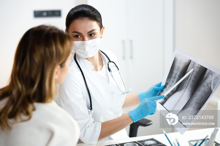 Calm pretty pediatrician in medical mask keeping x-ray photo of spine