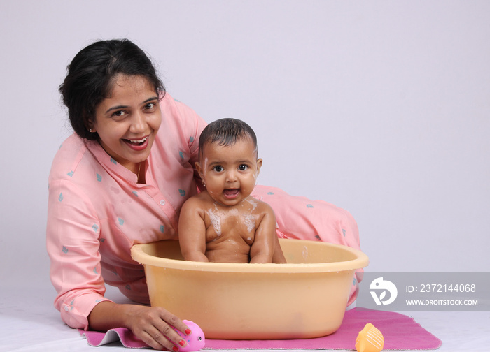 Cheerful Indian mother giving bath to baby.